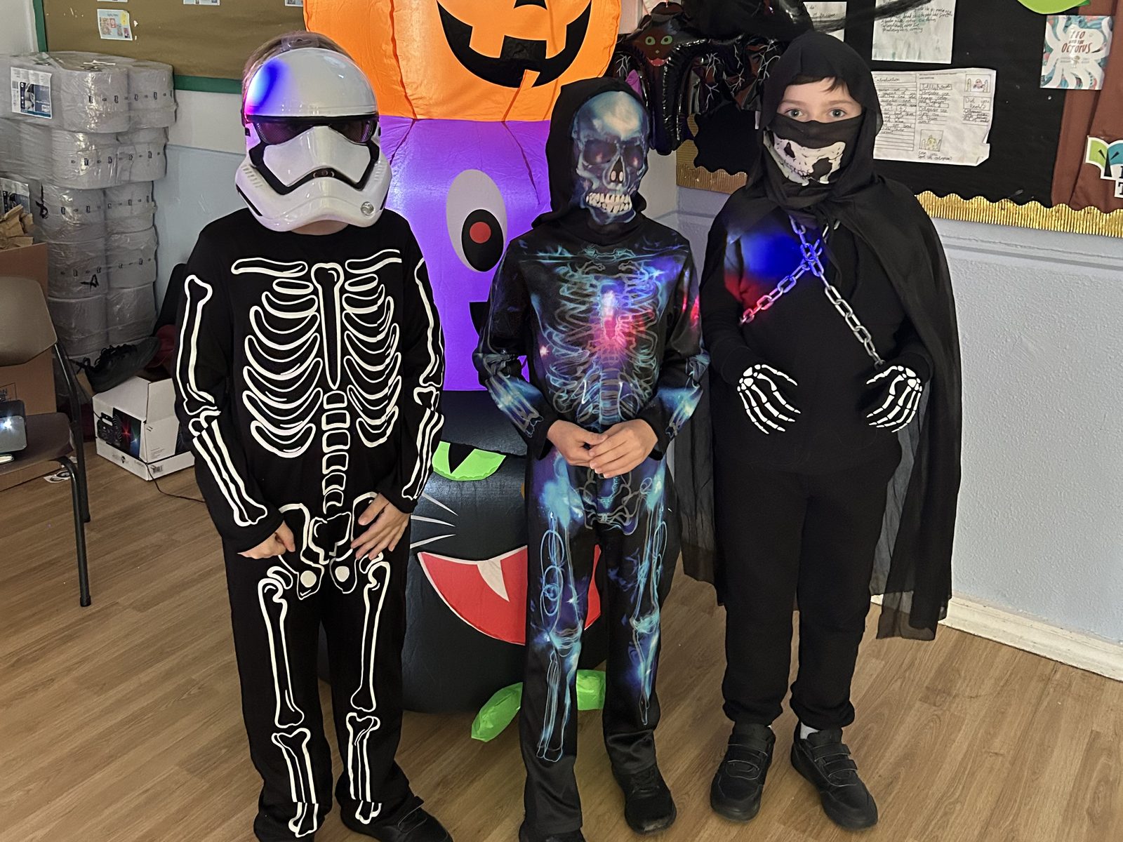 Three children in Halloween costumes and masks in front of a giant inflatable ghost and pumpkin