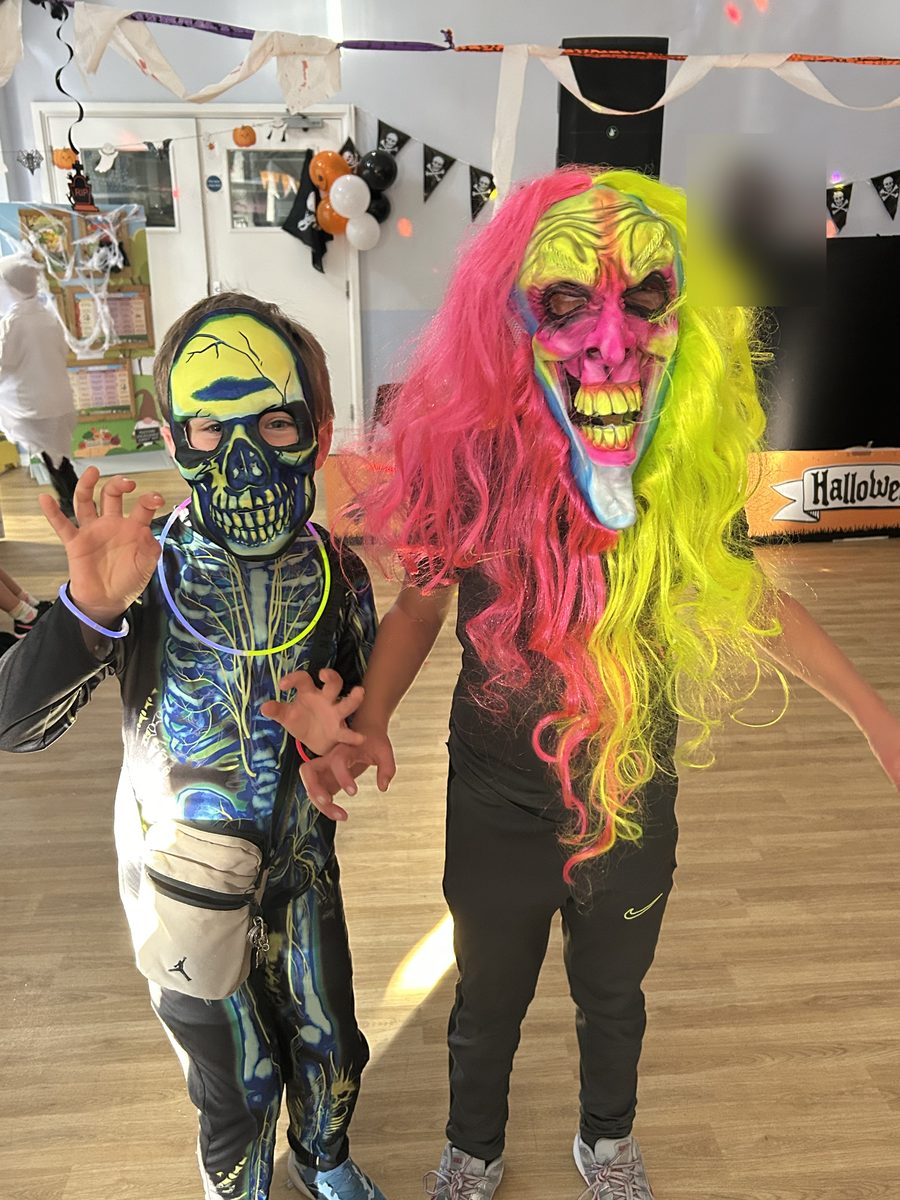 Two children in neon skull and monster masks, one with a long pink and yellow wig