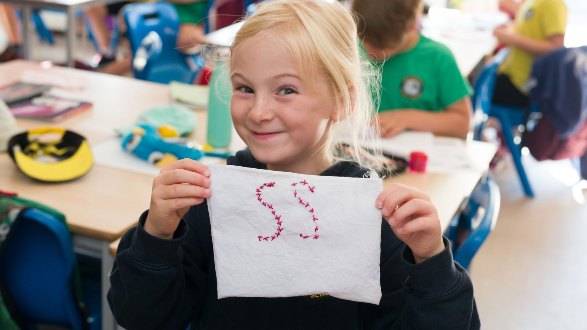 A Swiss Gardens pupil holding up an embroidered fabric square showing the school initials